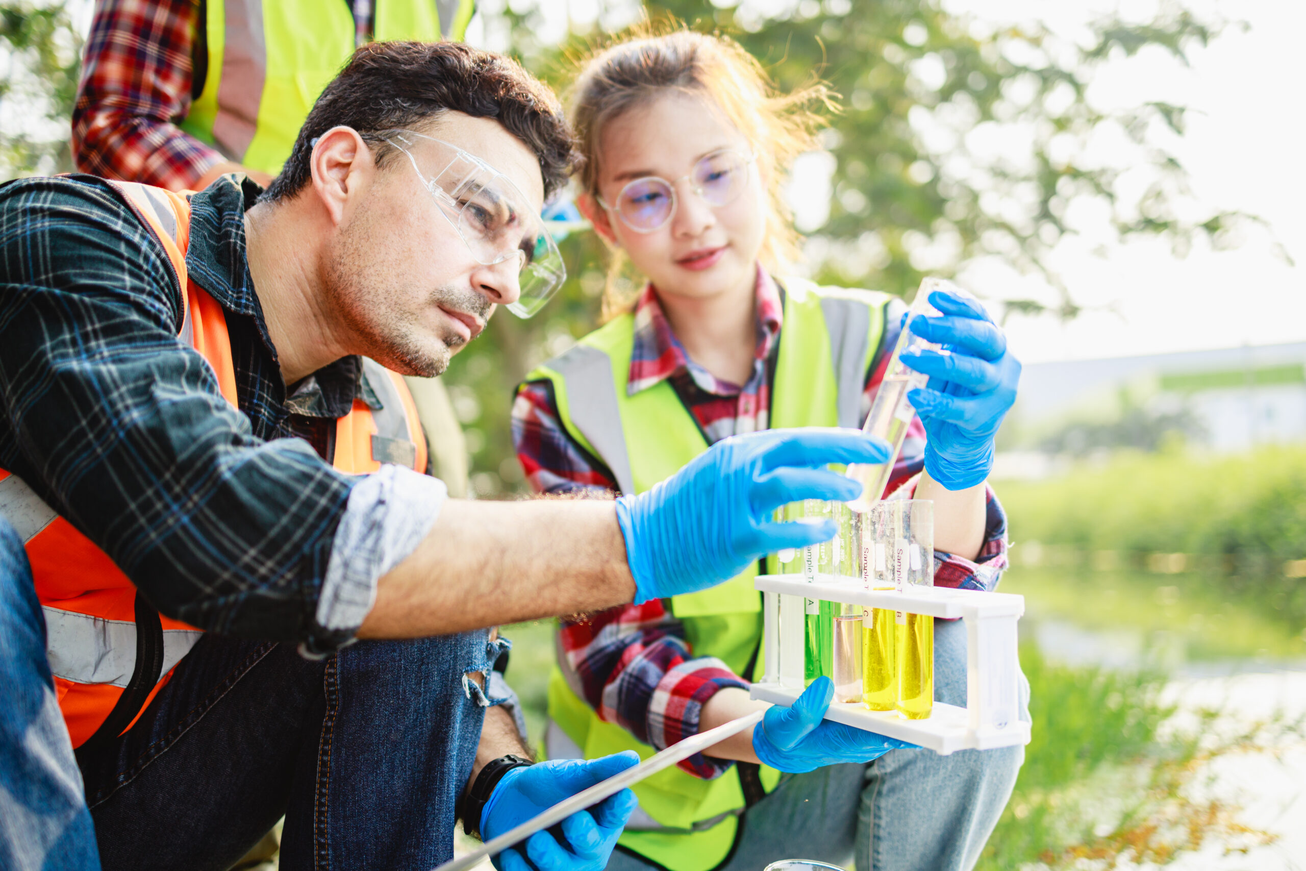 a man and woman in safety vests looking at test tubes - environmental science assignment help